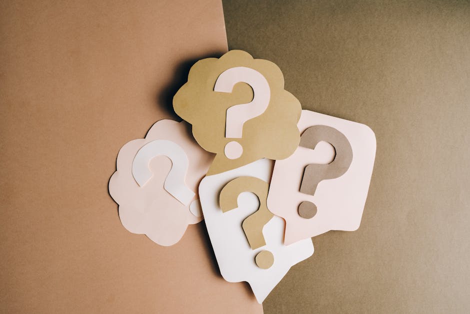 Multiple paper cutouts of speech bubbles with question marks are arranged on a background divided into two shades of brown, one darker and one lighter. The speech bubbles are in cream and light brown colors, overlapping each other, symbolising confusion or questions. The setting appears to be indoors, with the paper elements placed on a flat surface used for visual composition. This image visually represents querying or uncertainty, which can relate to clarifying costs and procedures in house removals. To support home relocation and furniture transport services, Man with Van Berrylands may use such imagery to address common client questions about moving costs, packing, and logistics as referenced in the page about determining removal pricing, aligning with themes of moving services and packing and moving processes.
