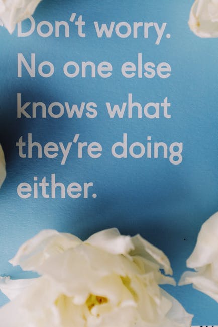 The image shows a close-up view of a light blue wall with a motivational quote printed in large, white, and grey letters stating, 'Don't worry. No one else knows what they're doing either.' Below the quote, there are white flowers with soft petals arranged at the bottom of the image. In the context of house removals, the background suggests an interior environment, possibly a decorated wall in a living space or office, reflecting a calm or reassuring atmosphere. The focus on this wall and floral decoration does not directly depict furniture or moving activities but can imply a welcoming or tidy environment associated with a home or office used during or after relocation. The color scheme and decor suggest a neat, prepared space, aligning with the professionalism of a removals and packing service provider like Man with Van Berrylands. This visual detail can be relevant in an article about packing, moving logistics, or home relocation, especially when emphasizing the importance of organized and stress-free moves.